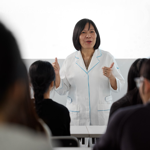 一位穿着白色实验室外套的讲师在满是学生的教室中授课