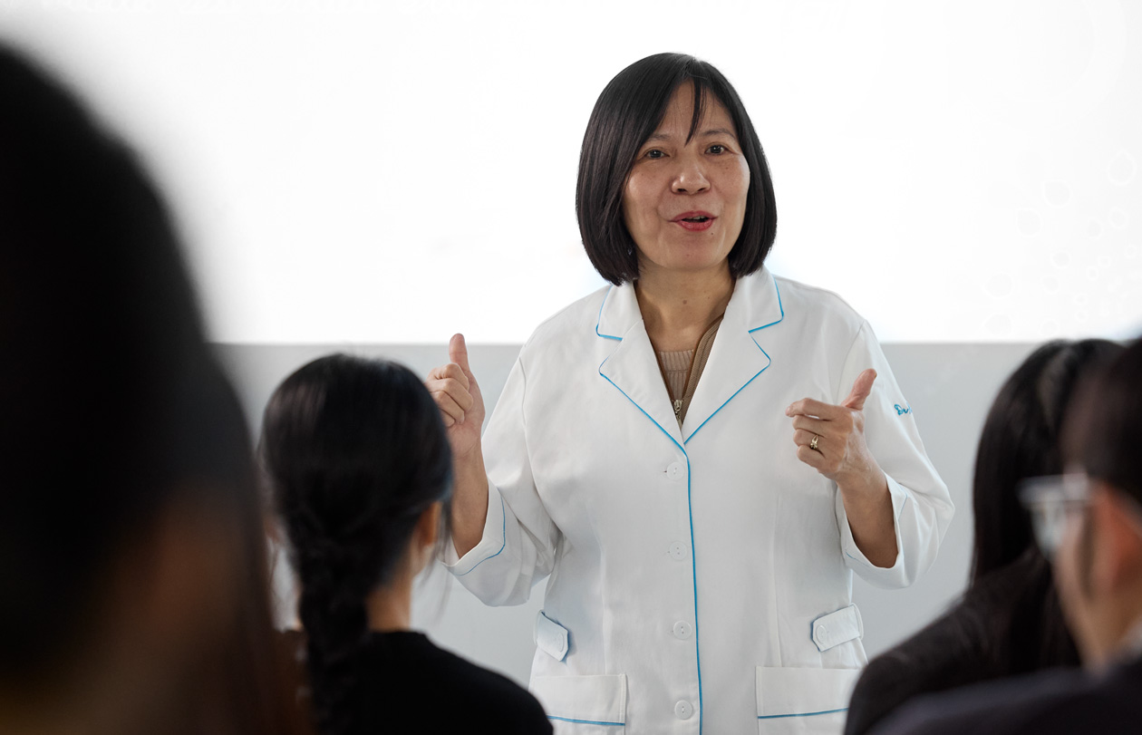 一位穿着白色实验室外套的讲师在满是学生的教室中授课