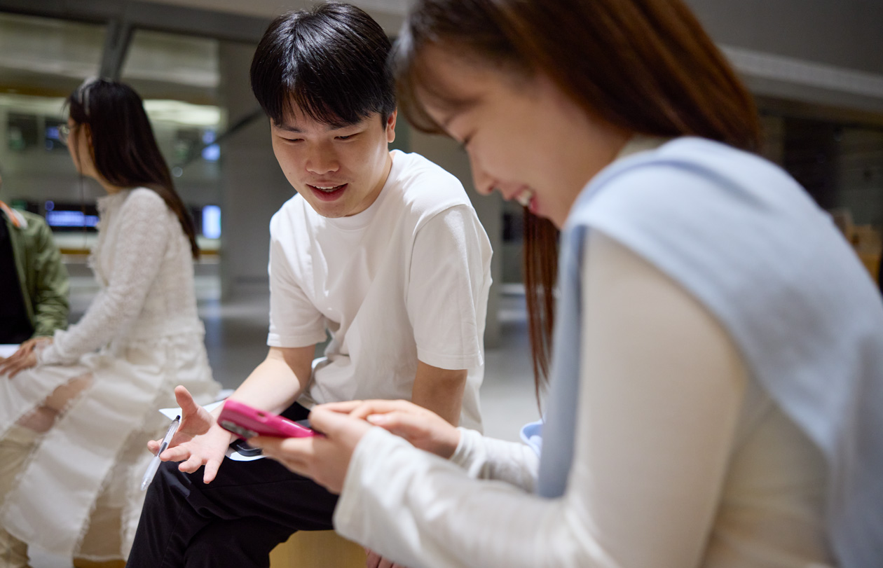 两个人边交谈边低头看着 iPhone，iPhone 由其中一个人拿着并操控