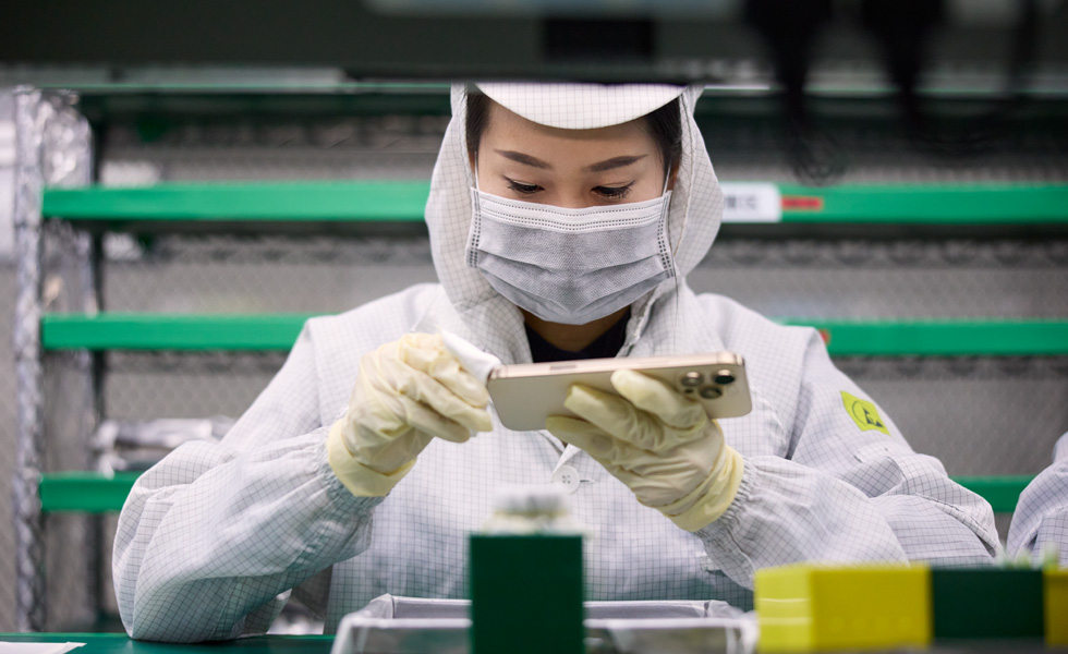 一名穿着全罩式工作服的员工在工作台前用布擦拭 iPhone