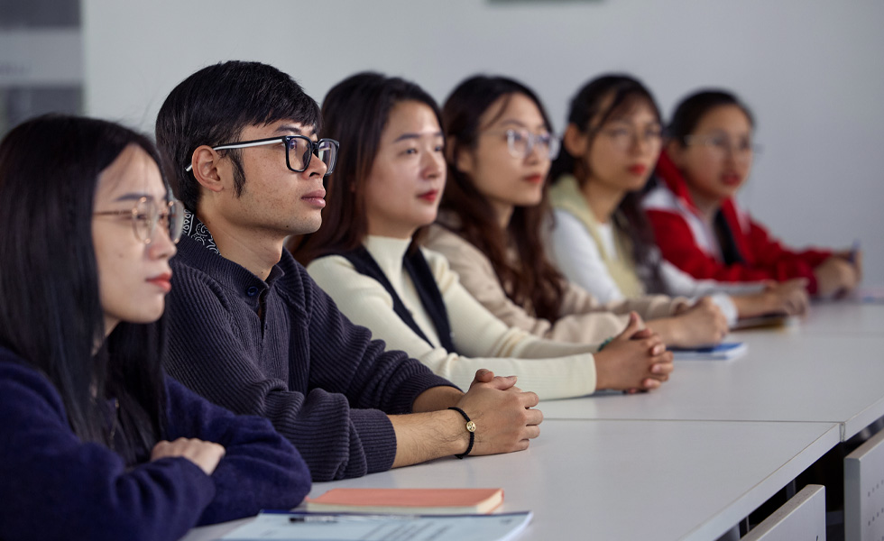 六个人坐在一排长桌前，专注于教室前方